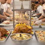 Cozinheiros preparando ceia de Natal por encomenda com pratos tradicionais, como peru, tender e saladas, em uma cozinha profissional.